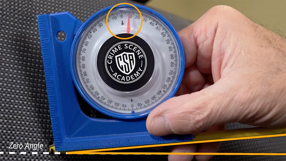 Close-up of an angle finder being used to measure the vertical impact angle of a bullet defect.